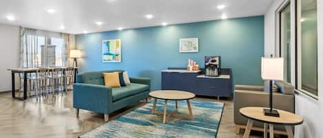 A modern living room with a blue wall, a green sofa, a round coffee table, and a dining area with chairs and a table.