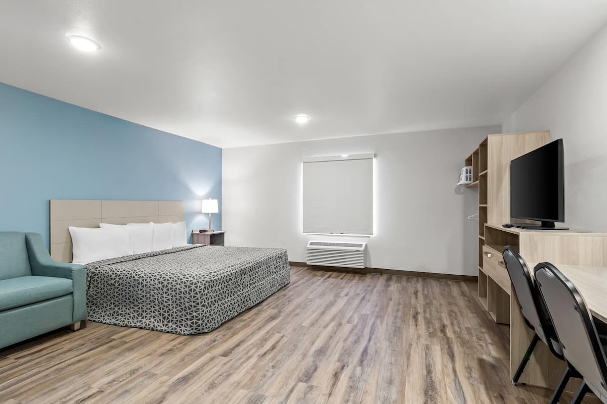 A modern hotel room with a bed, a desk, a TV, and a blue accent wall.