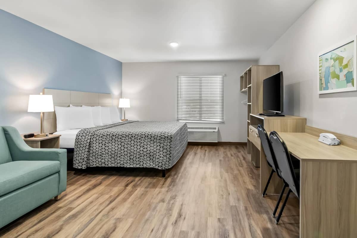 A hotel room with a bed, desk, chair, TV, and artwork on the wall.