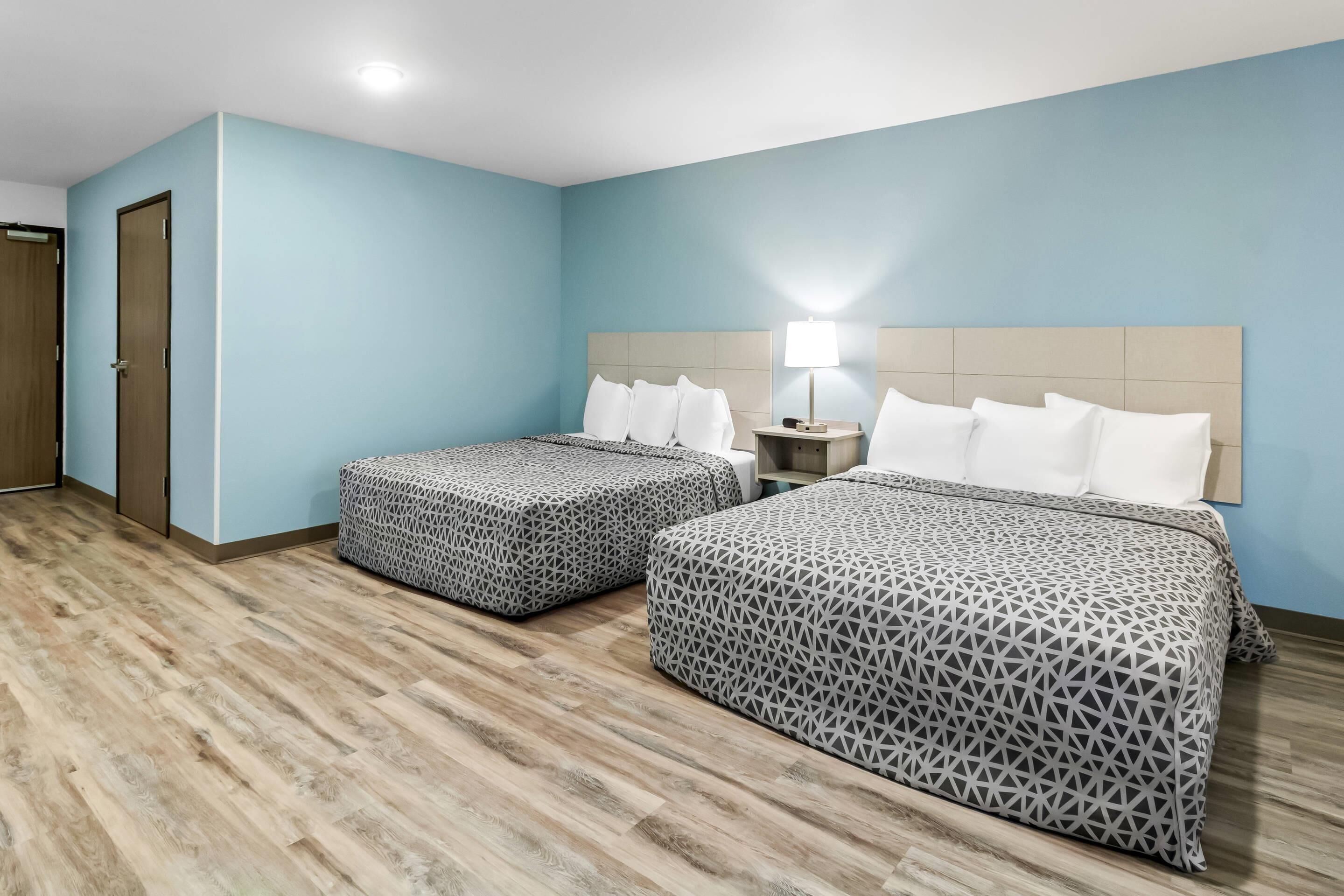 A hotel room with two beds, a nightstand with a lamp, and a wooden floor.