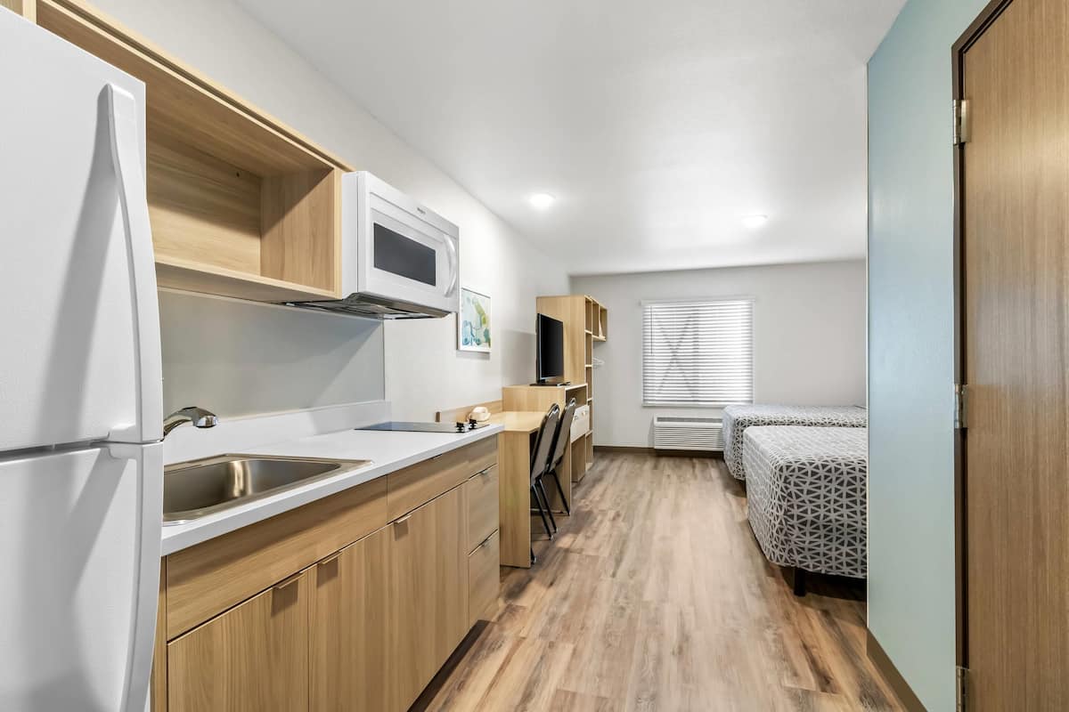 A compact kitchen with a microwave, sink, and wooden cabinets. There is a small seating area with a table and chairs.