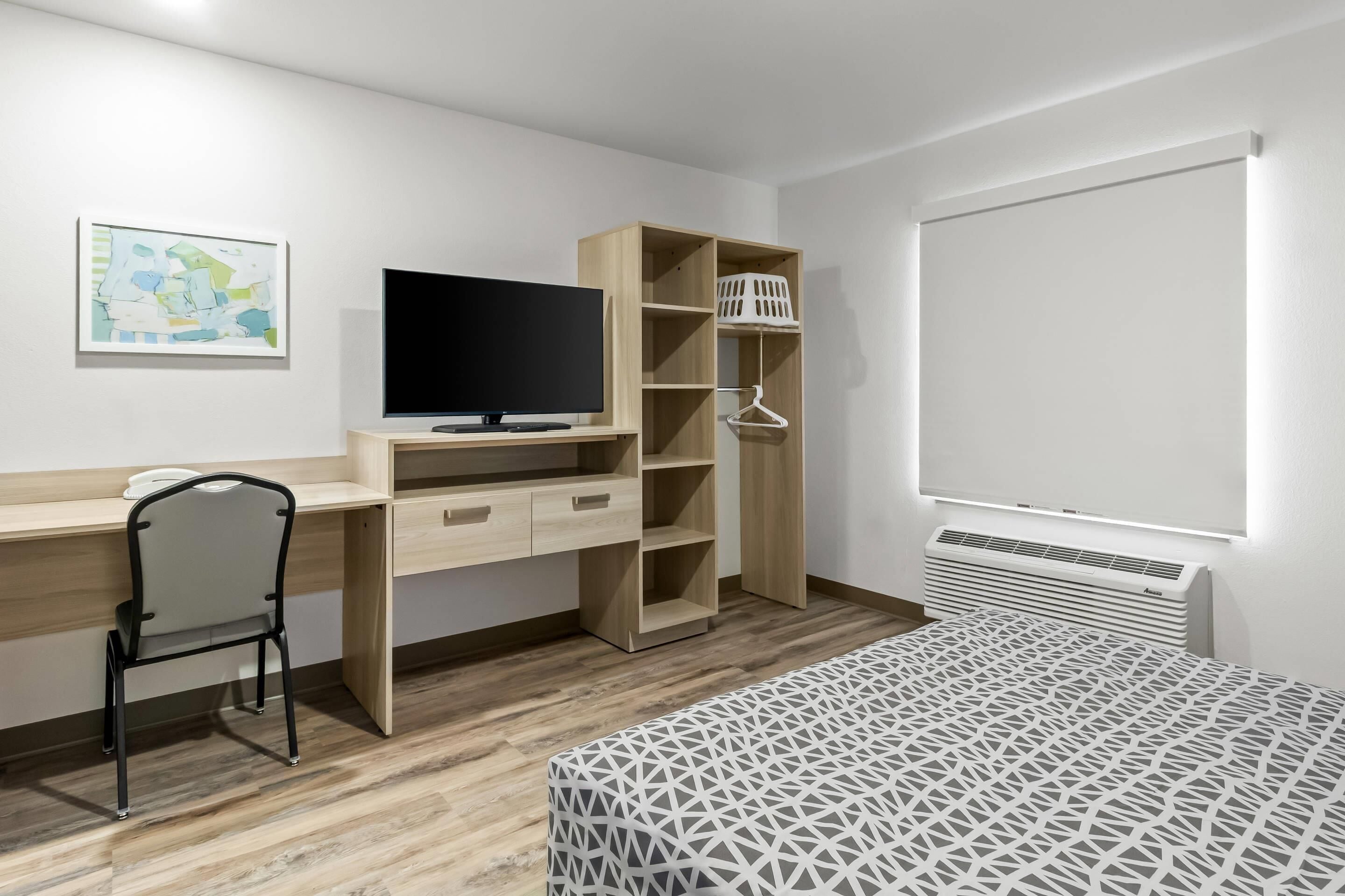 A bedroom with a bed, a desk with a chair, a television, a wardrobe, and a window.