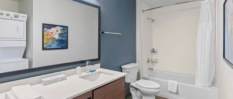 A modern bathroom with a large mirror, dual sinks, a toilet, and a bathtub.