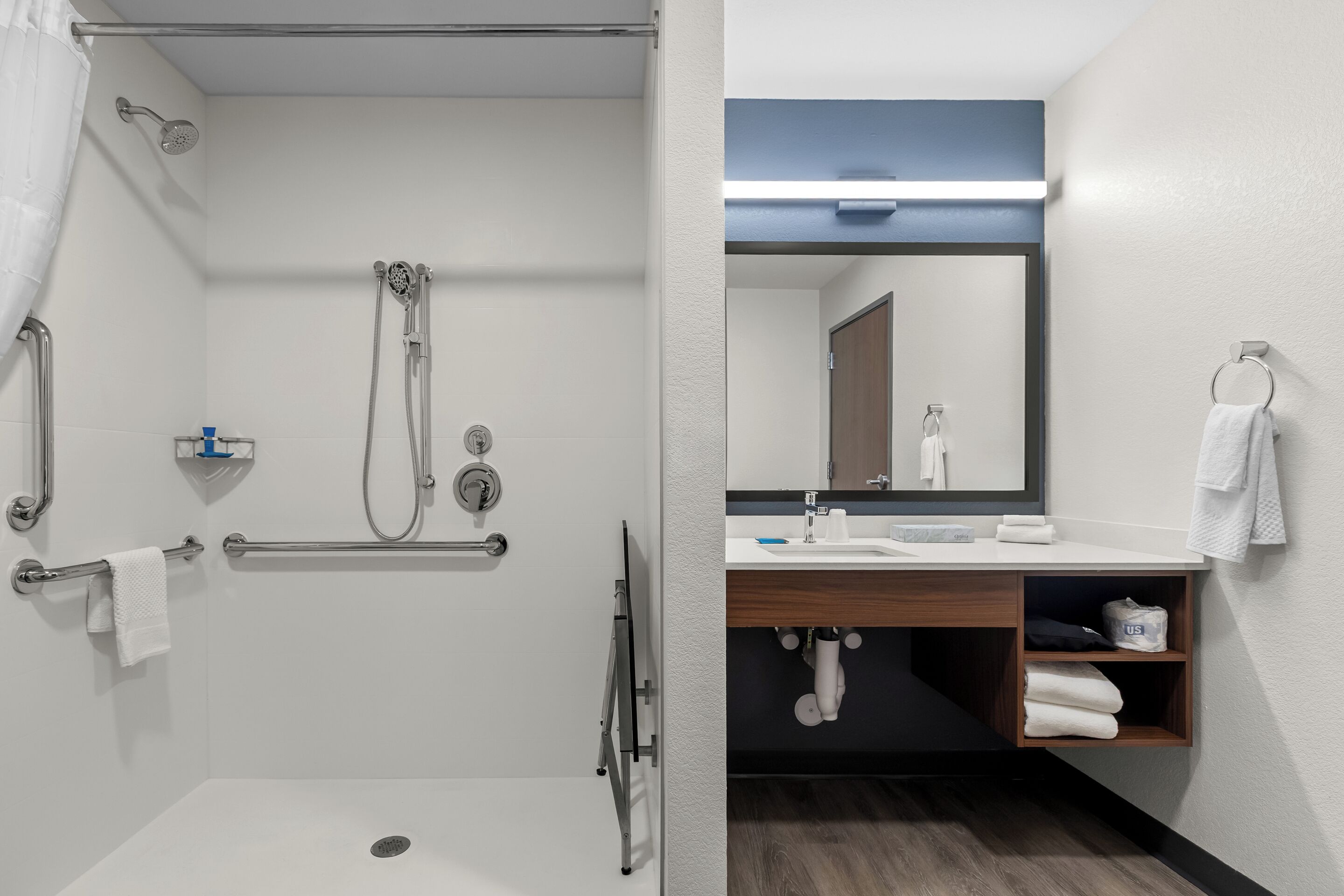 Een moderne badkamer met een douche, handgrepen, een wastafel en een spiegel.