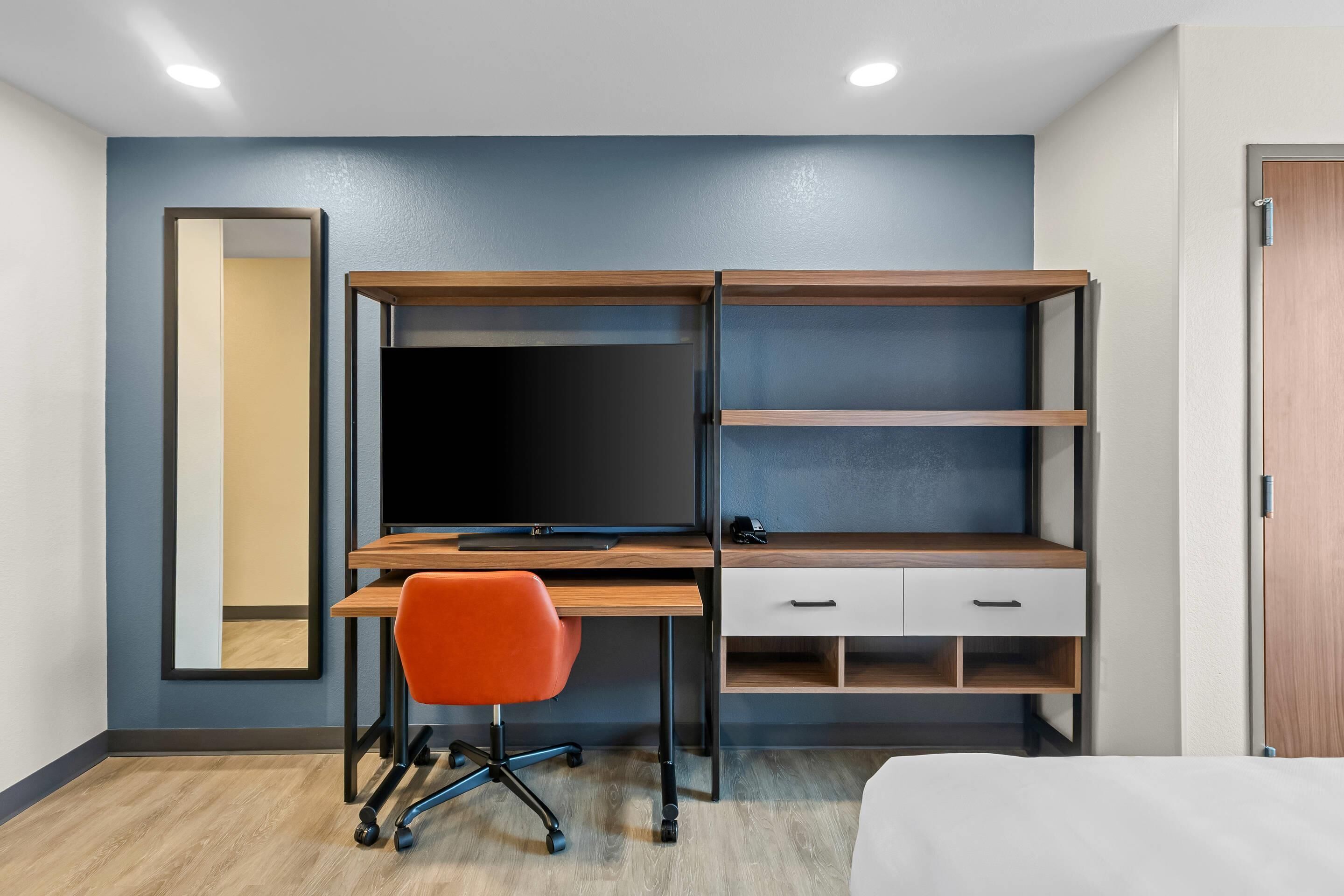 A modern bedroom with a wooden desk, a chair, a bed, and a wardrobe.