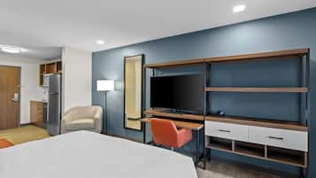 Une chambre d’hôtel comprenant un lit, un bureau avec une chaise, une télévision, un miroir et une kitchenette.