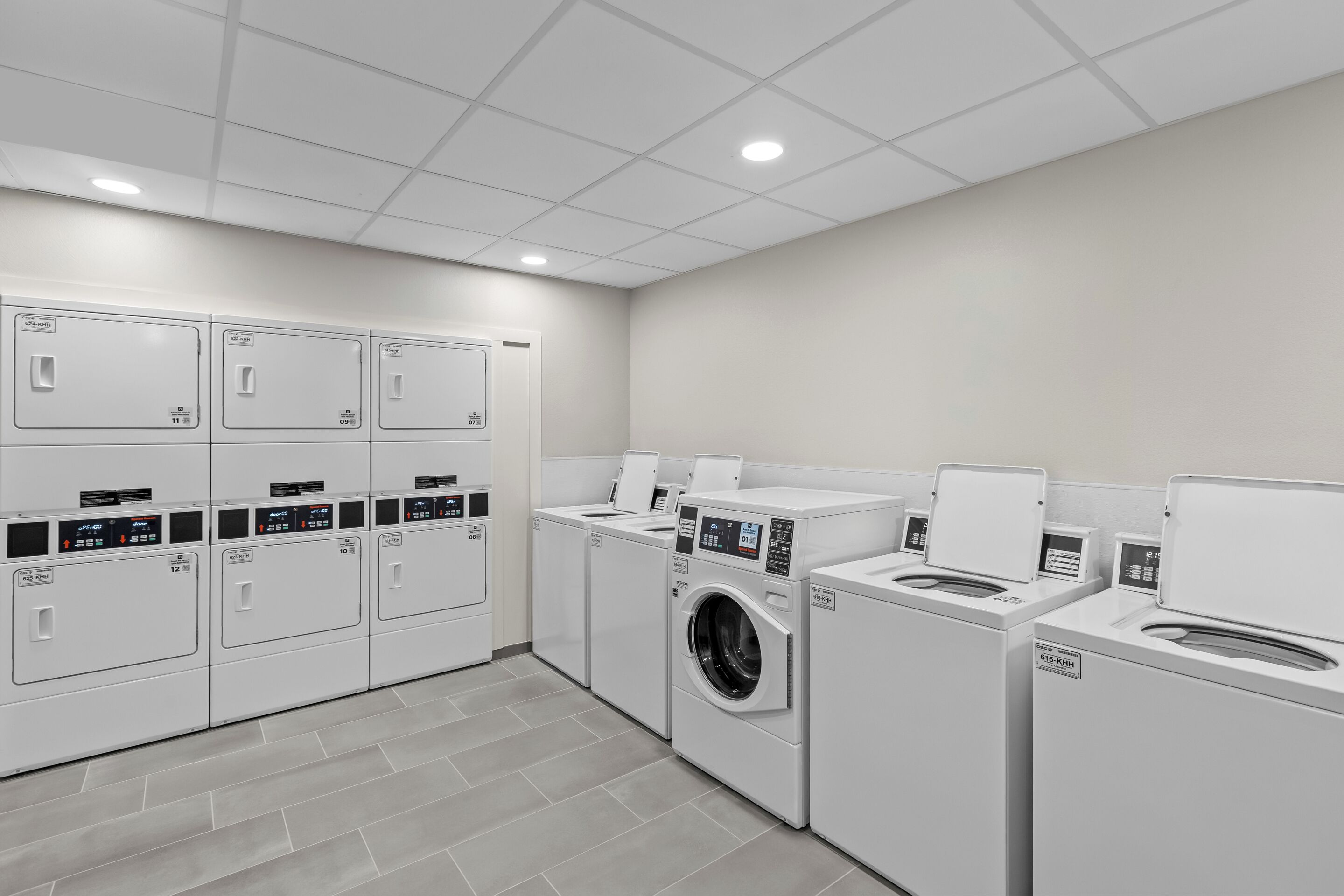 A modern laundry facility with multiple washing machines and dryers, a tiled floor, and a clean, well-lit environment.