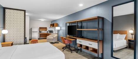 Habitación de hotel con cama, escritorio, silla, televisor y un espejo grande.