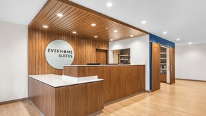 Een receptiebalie met een bordje dat 'EVERHOME SUITES' vermeldt, in een modern interieur met houten lambrisering en inbouwverlichting.