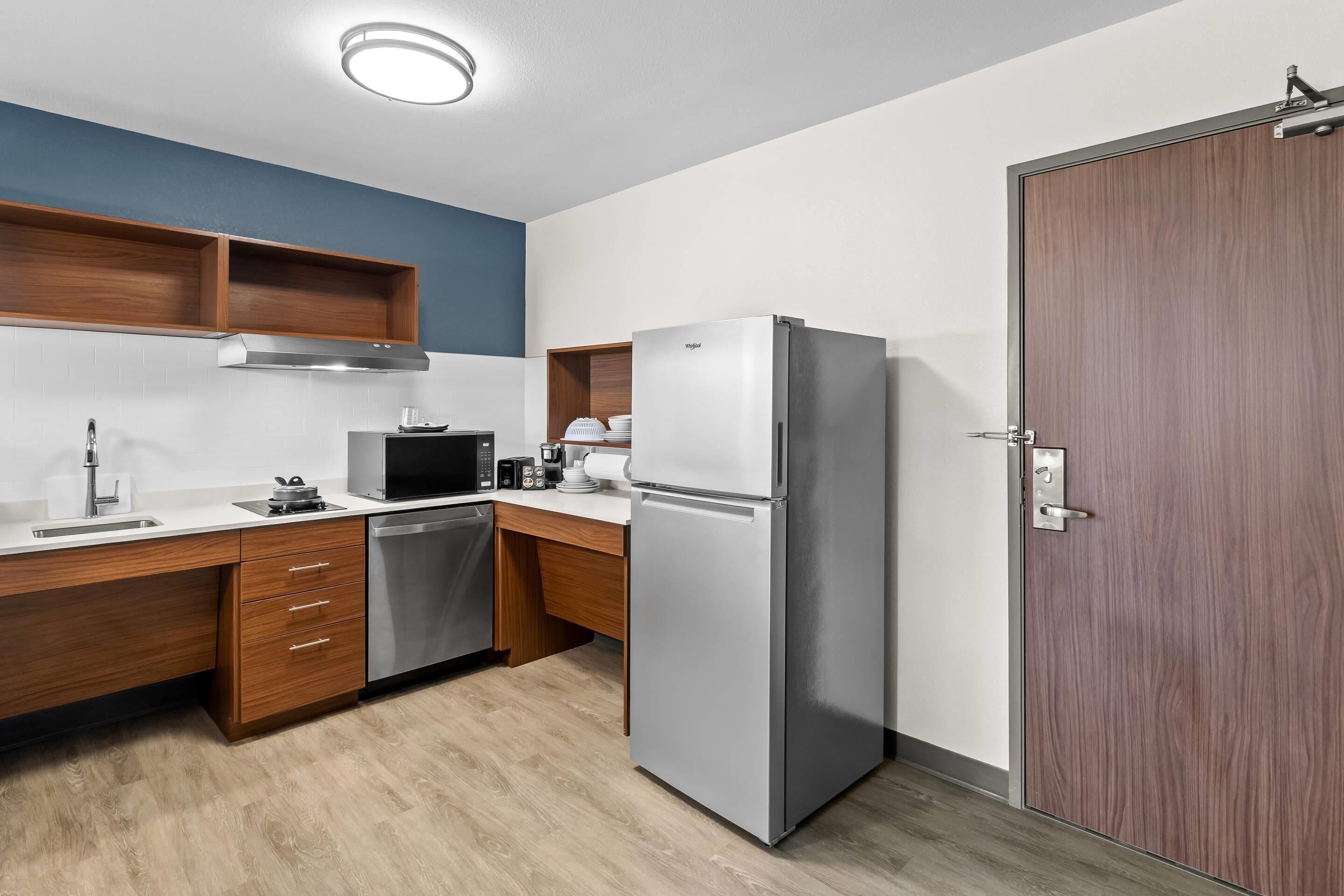 A modern kitchen with a stainless steel refrigerator, a microwave, and a dishwasher. There are wooden cabinets and a wooden countertop.
