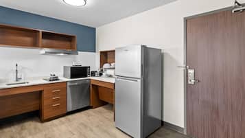 A modern kitchen with a stainless steel refrigerator, a microwave, and a dishwasher. There are wooden cabinets and a wooden countertop.
