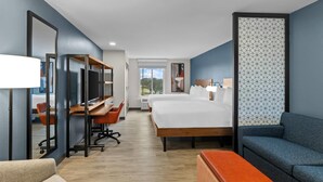 Een hotelkamer met een bed, een bureau met een computer, een stoel, een bank en een grote spiegel.