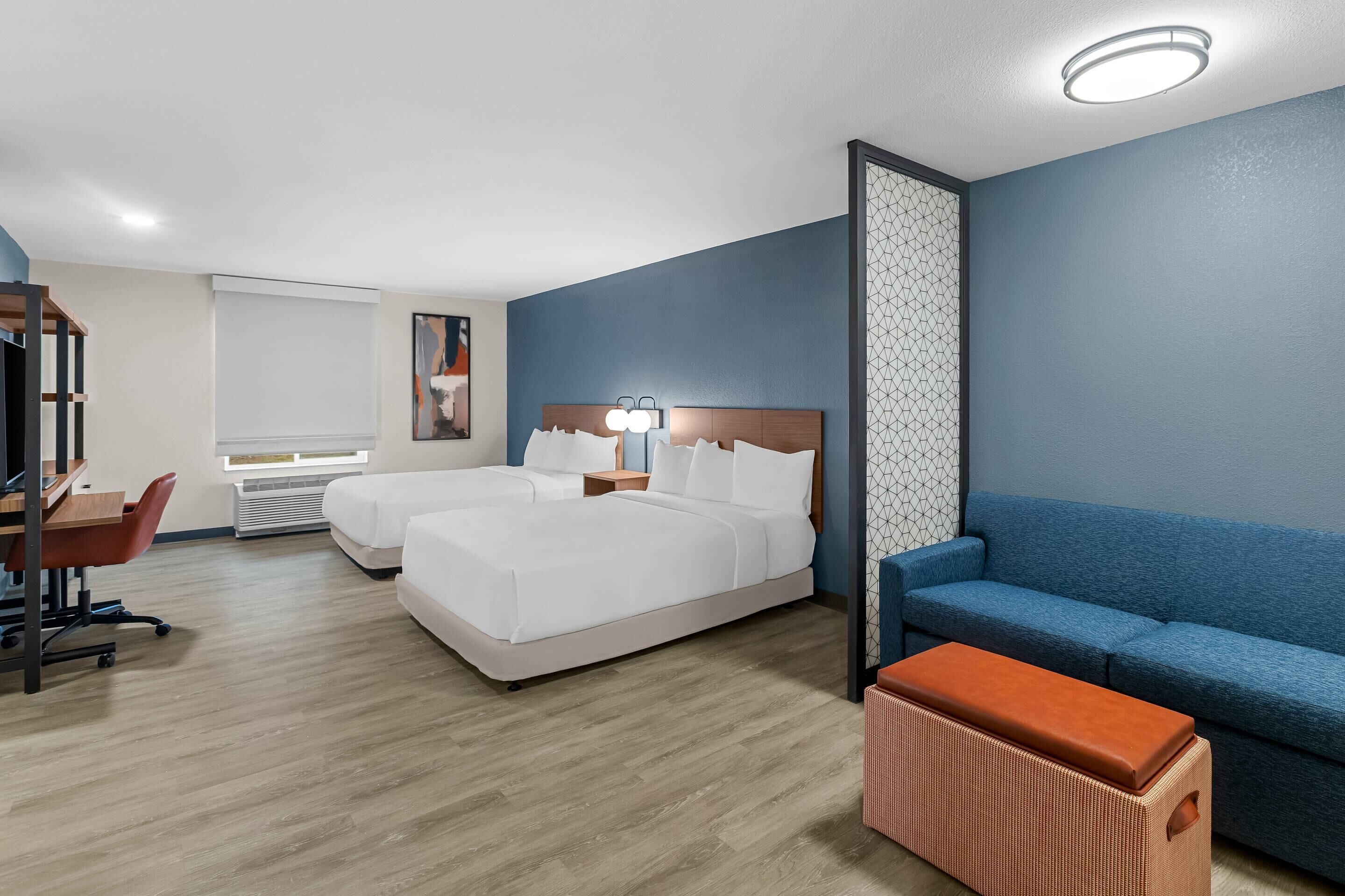 Una habitación de hotel con cama, escritorio, silla, sofá azul y una mesita.