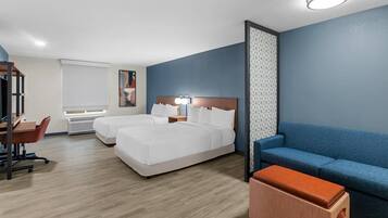 Una habitación de hotel con cama, escritorio, silla, sofá azul y una mesita.