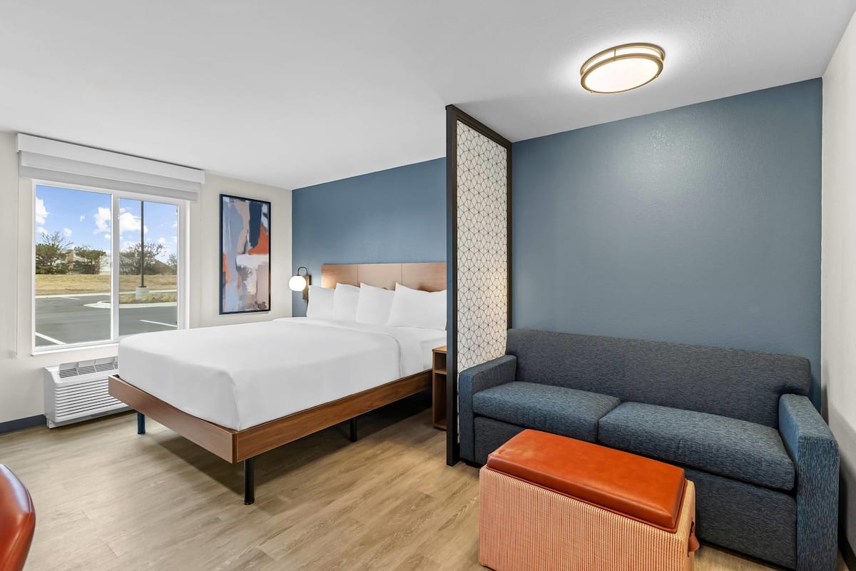 A hotel room with a bed, a sofa, a small table, and a window with a view of the outdoors.