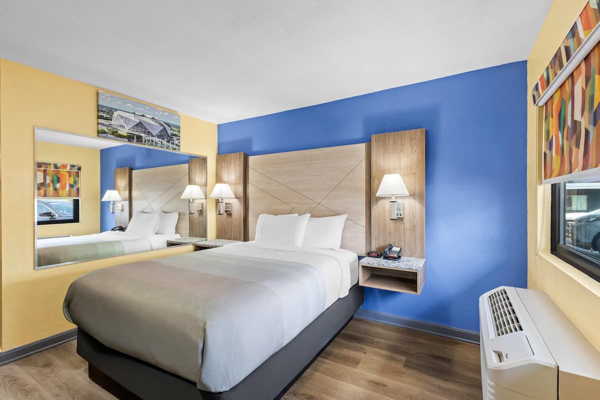 A hotel room with a large bed, bedside lamps, a mirror, a TV, and an air conditioning unit.