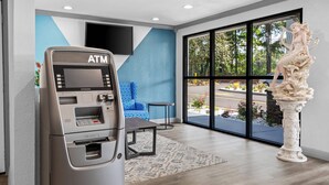An ATM, a blue patterned sofa, and a statue in a modern room with large windows. - Quality Inn & Suites East Point - Atlanta Area (Atlanta)