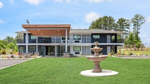 A modern two-story building with a covered entrance, a fountain in the front lawn, and a view of the surrounding landscape. - Quality Inn & Suites East Point - Atlanta Area (Atlanta)