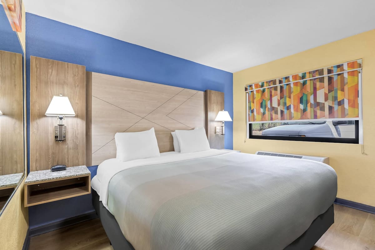 A hotel room with a bed, bedside lamps, a nightstand, a painting, and a window.