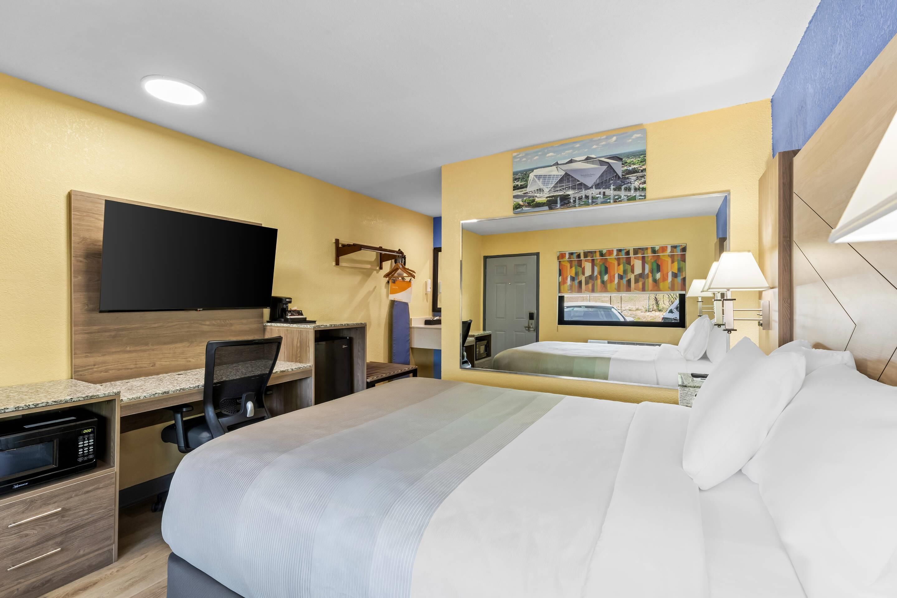 A hotel room with a bed, desk, chair, television, and a mirror.