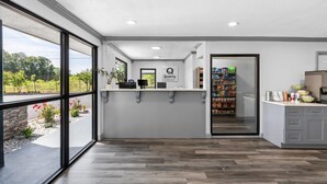 A reception area with a counter, a sign reading 'Quality Baby,' and a view of a garden through large windows. - Quality Inn & Suites East Point - Atlanta Area (Atlanta)