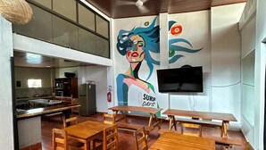 Un espace repas avec des tables et des chaises en bois, une fresque murale et un téléviseur fixé au mur.