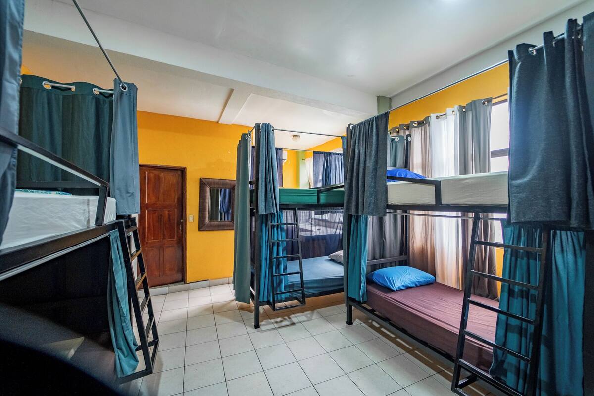 A dormitory room with bunk beds, curtains, and a wooden door.