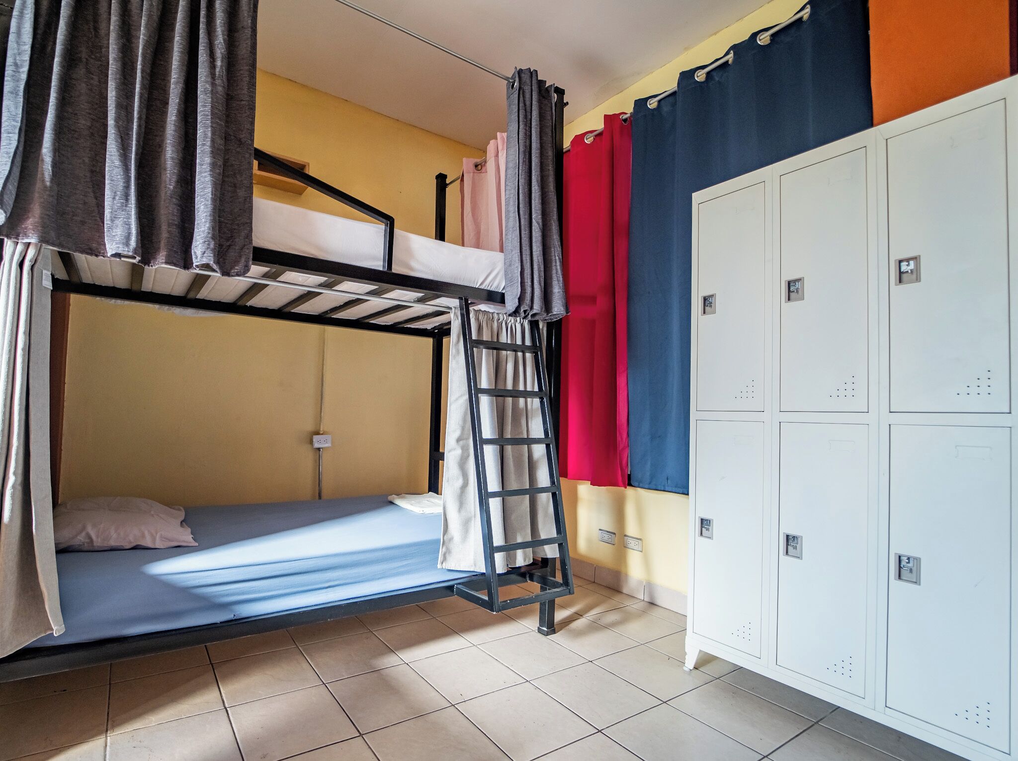 A bunk bed room with a ladder, a wardrobe, and a wall with a curtain.