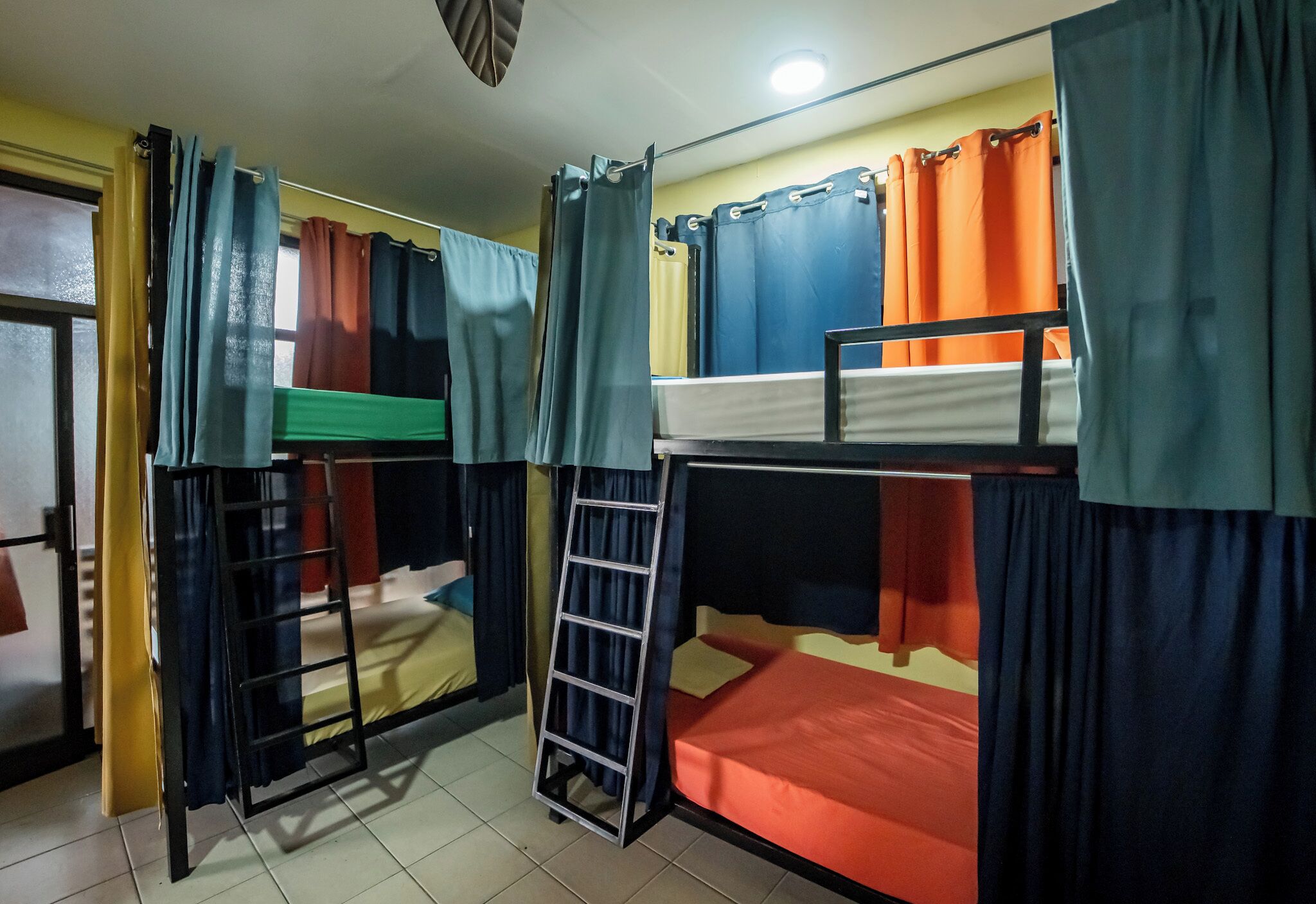 A dormitory room with bunk beds, curtains, and a ladder.