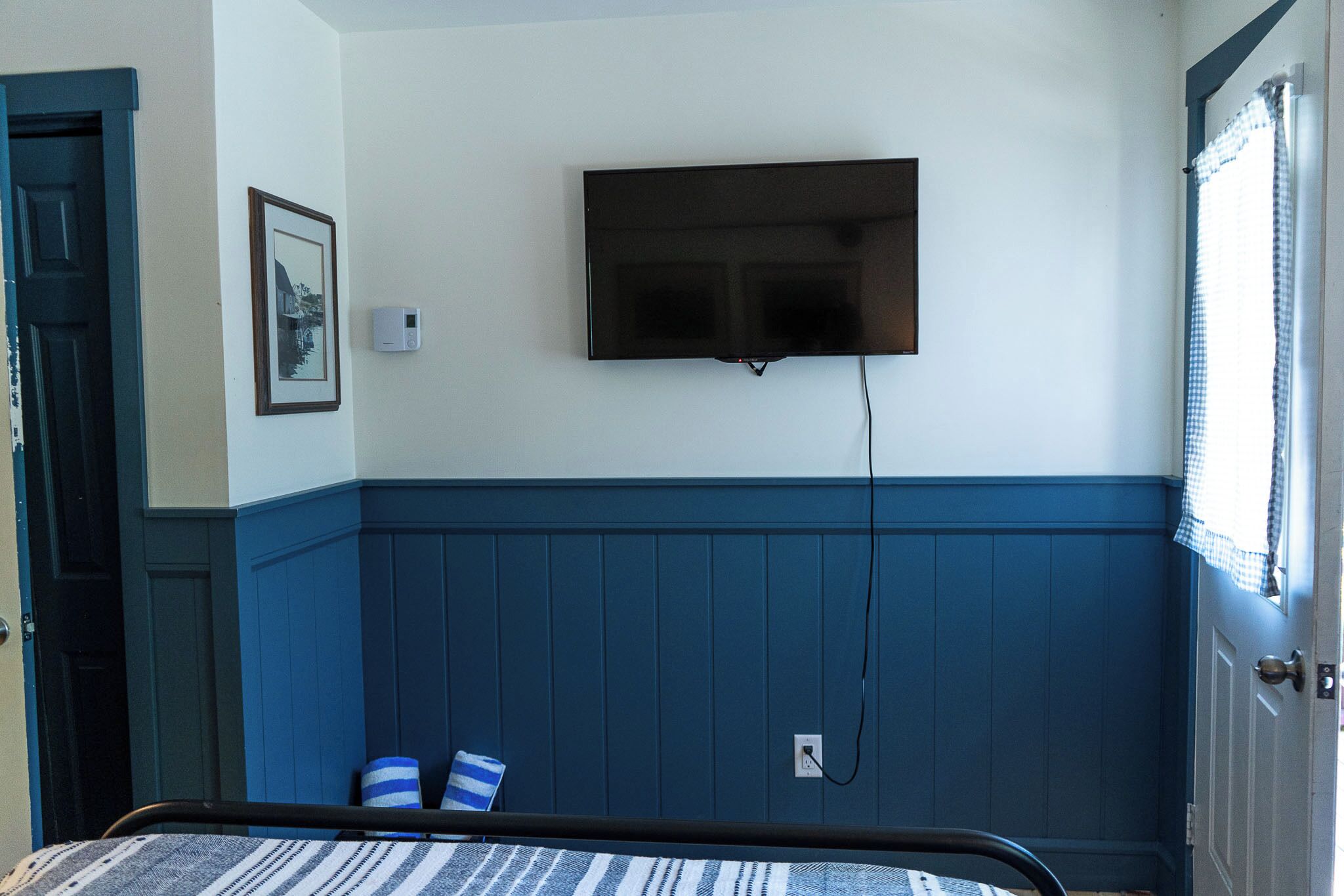 A room with a bed, a mounted television, a door, and a window with curtains.