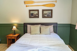 Un lit avec une couette, des oreillers, une table de chevet avec une lampe et deux tableaux encadrés accrochés au mur.
