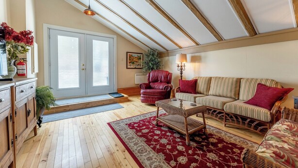Una sala de estar acogedora con piso de madera, un sofá estampado en rojo y beige, un sillón de cuero rojo, una mesa de centro de mimbre y un tapete rojo y beige.