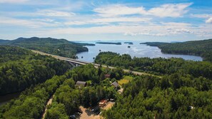 An aerial view of a forested area with a bridge, a lake, and a small settlement with houses and parked cars. - Large Suite in Historic Carriage House! Pet-Friendly! (Bocabec)