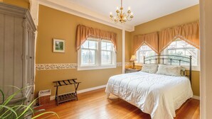 A bedroom with a bed, a wooden floor, a chandelier, and a window with curtains.