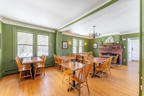 A dining area with wooden tables and chairs, a brick fireplace, and green walls.