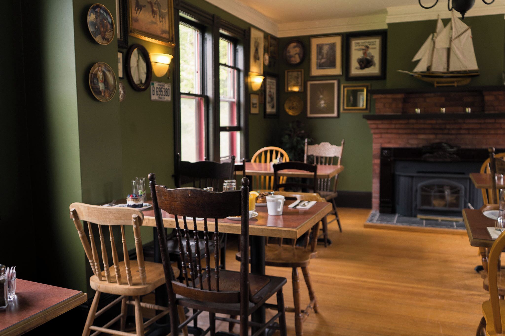 Un comedor con sillas y mesas de madera, cuadros en las paredes y una chimenea.