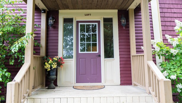 A purple door with a white porch and a flower pot on the steps.