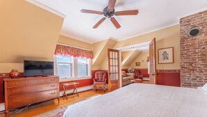 A bedroom with a bed, a dresser, a television, a ceiling fan, and a window with a valance. - Spacious Garden-View King Suite in 150-Year-Old Manor House (Bocabec)