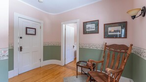 Une pièce avec un plancher en bois, un fauteuil à bascule, un tableau encadré accroché au mur et une porte ornée d’un petit certificat encadré.