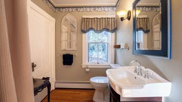 A bathroom with a white toilet, a white sink, a mirror, and a window with a view of trees.