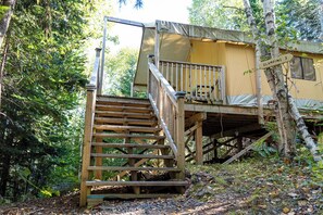 Une cabane en bois avec un escalier menant à une terrasse, entourée d’une forêt dense.