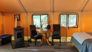 Una habitación con carpa, un estufa de leña, dos sillas, una mesa con lámpara y una cama.
