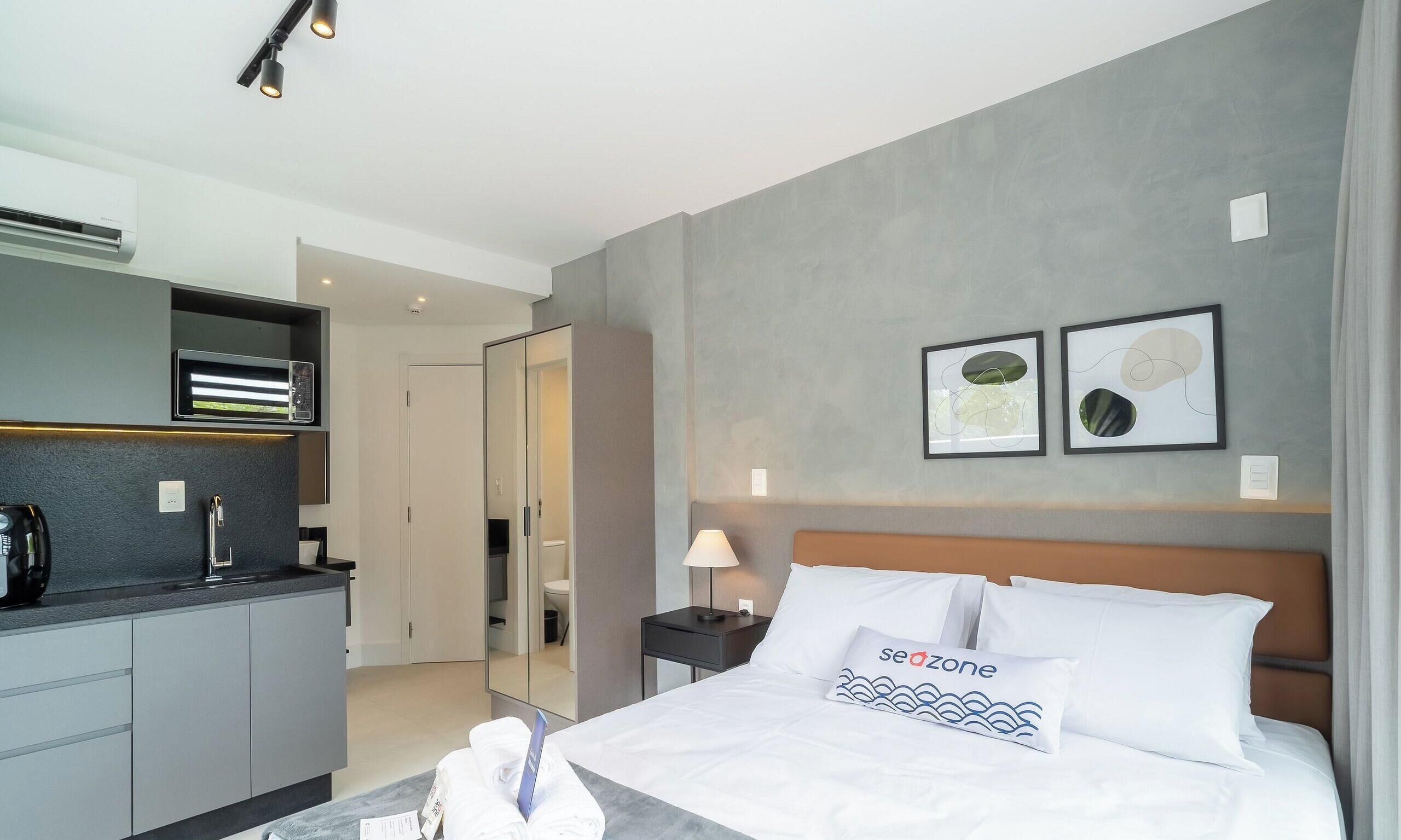 Una habitación de hotel moderna con una cama, una mesita de noche, una lámpara, un espejo, un armario y una kitchenette.