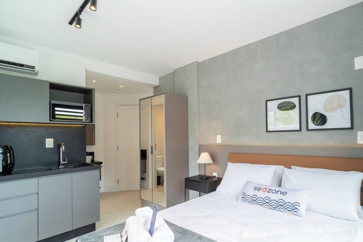 Une chambre d’hôtel moderne équipée d’un lit, d’une table de chevet, d’une lampe, d’un miroir, d’une armoire et d’une kitchenette.