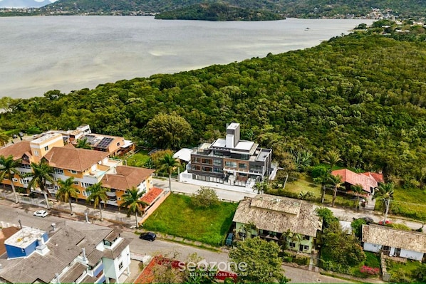 Vista aérea de un pueblo costero con una mezcla de edificios modernos y tradicionales, una extensa masa de agua y vegetación exuberante.