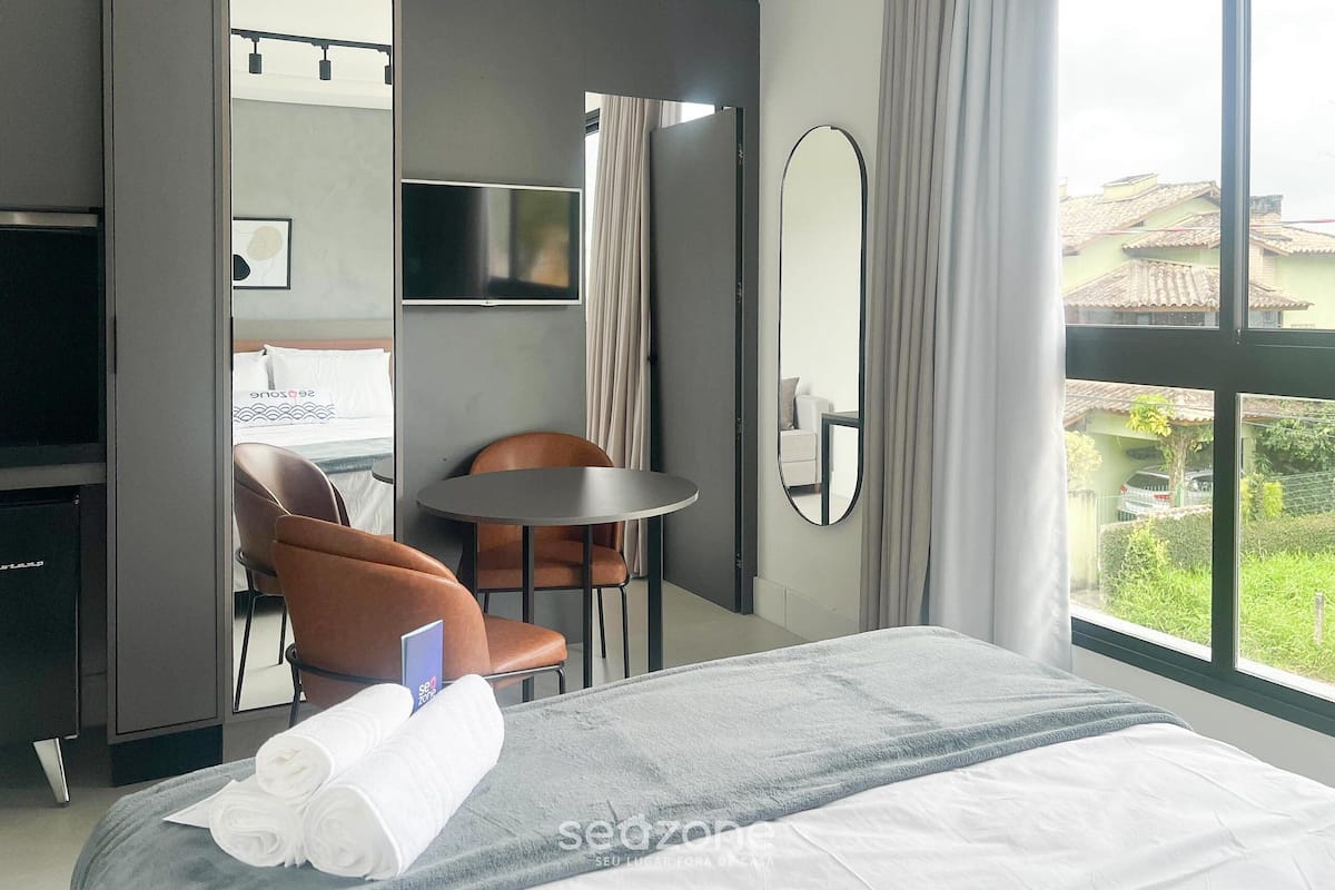 A hotel room with a bed, a TV, a desk, a chair, a round table, and a view of the outside.
