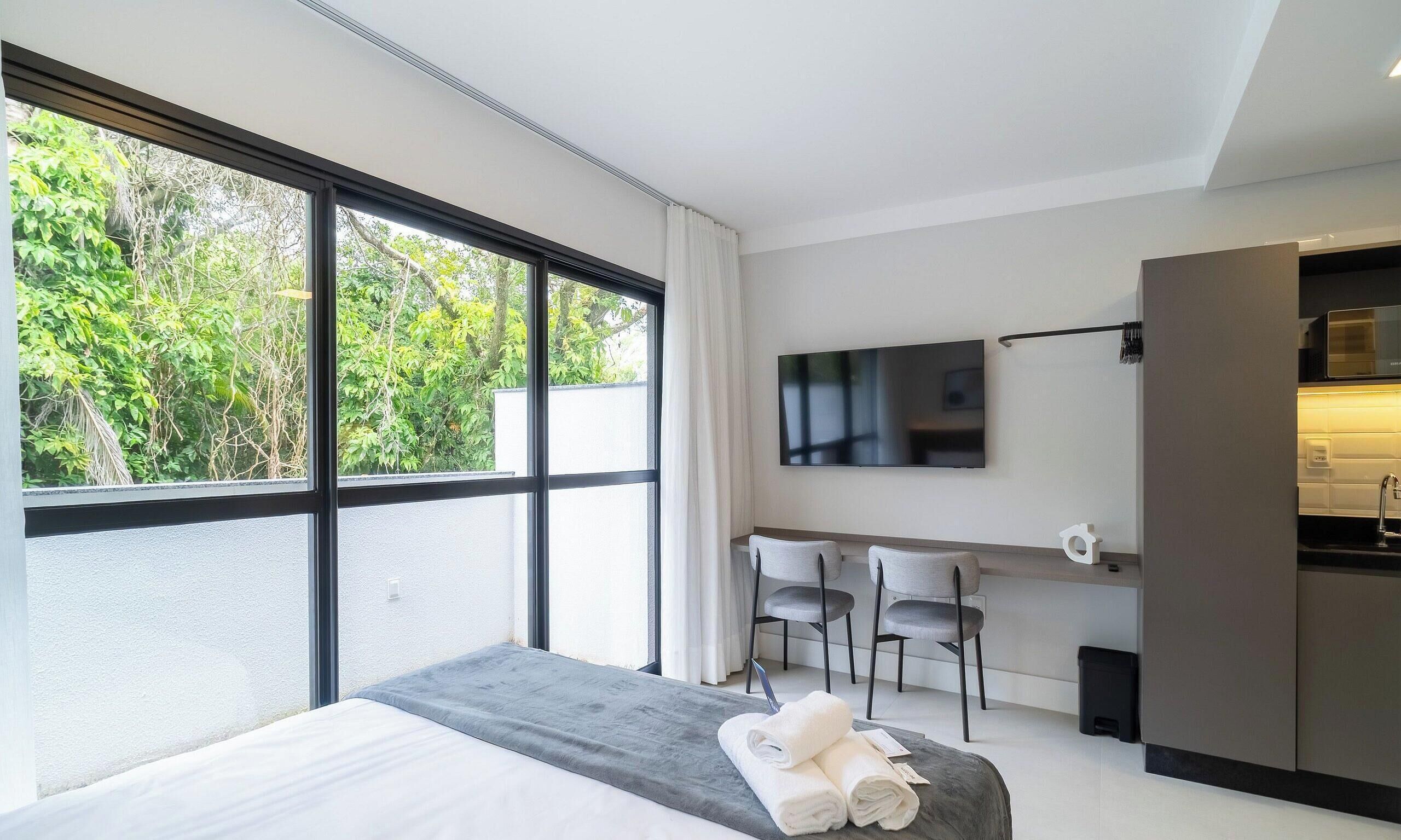 Una habitación de hotel moderna con un ventanal grande, una cama, un televisor y una kitchenette.