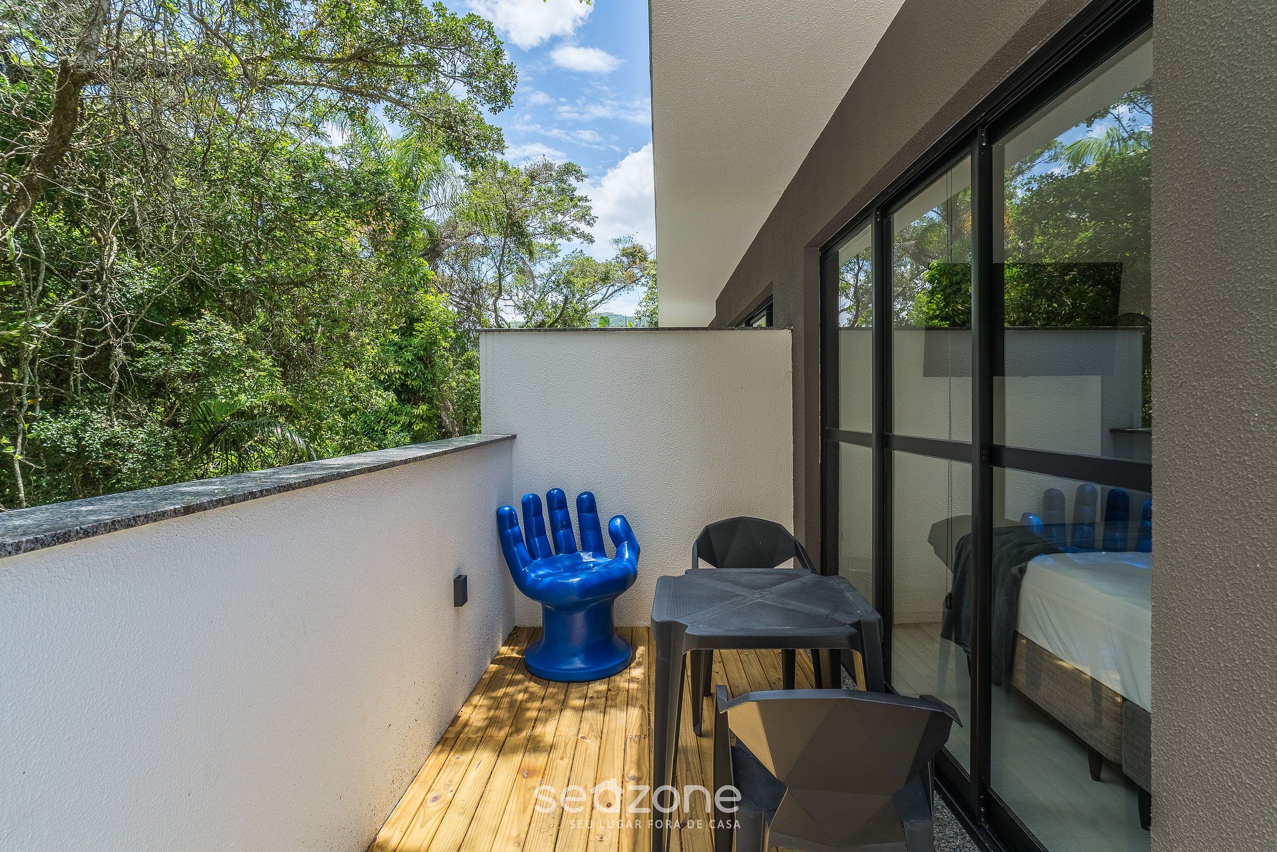 Un balcon avec un plancher en bois, une chaise bleue, une petite table et un lit recouvert d’une courtepointe blanche.