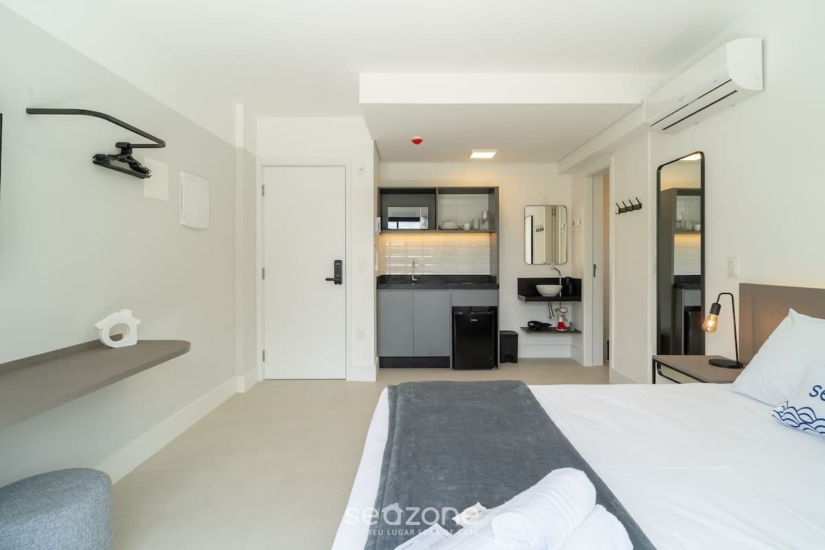 A hotel room with a bed, a desk, a chair, a small kitchenette, and a bathroom.