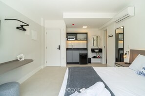 Habitación de hotel con cama, escritorio, silla, kitchenette pequeña y baño.